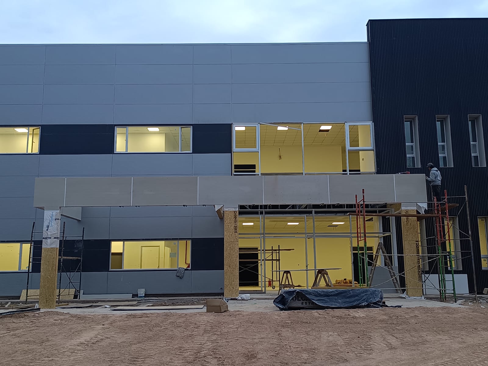 Obra institucional con fachada de paneles grises y acceso en ejecucion